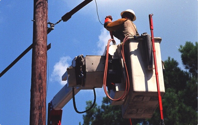 Persona en un elevador usando casco y trabajando con líneas eléctricas